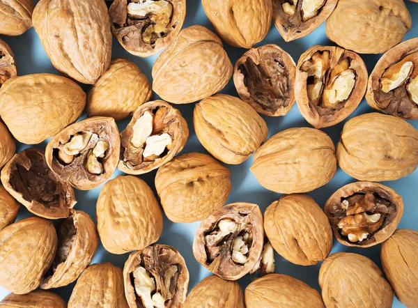 Walnuts whole in their skins, chopped on blue background — Stock Photo, Image