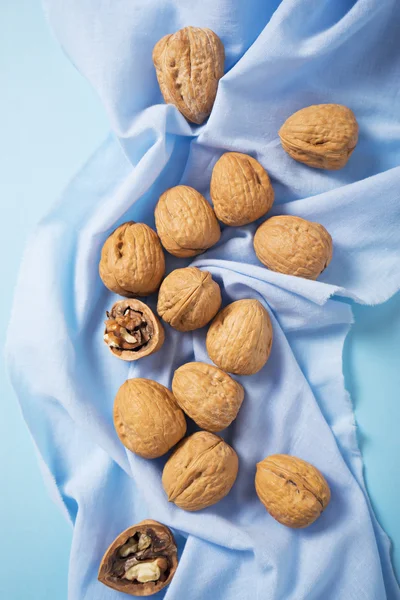 Walnuts whole in their skins, chopped on blue background — Stock Photo, Image