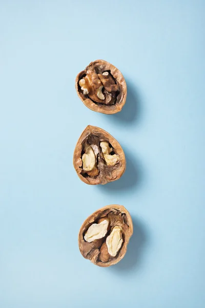 Walnuts whole in their skins, chopped on blue background — Stock Photo, Image