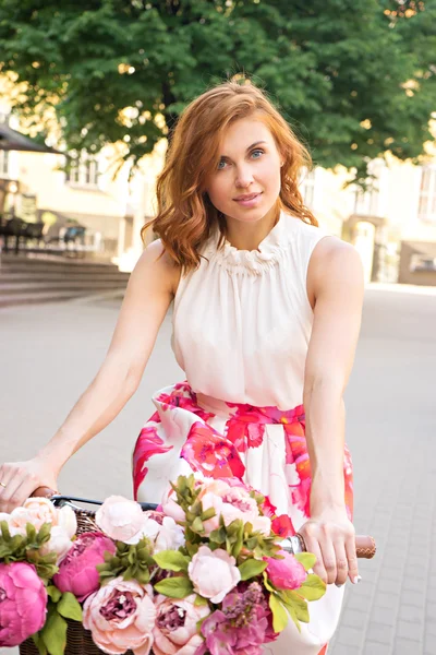 Belle femme avec vélo vintage et fleurs dans le panier — Photo