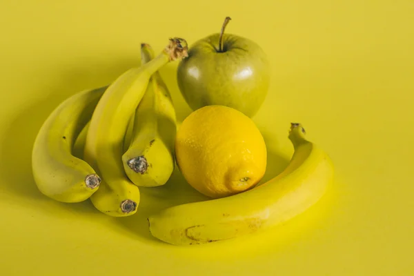 Bananer äpple och citron på gul bakgrund — Stockfoto