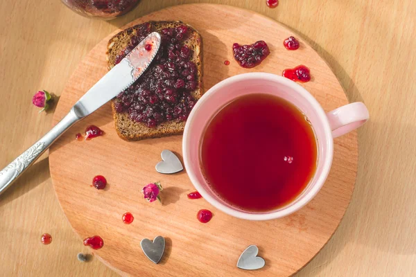 Cup of tea, fresh baked healthy bread with blackcurrant jam - homemade marmalade with fresh organic fruits from garden. In rustic decoration, fruit jam on wooden table background,sweet breakfast.