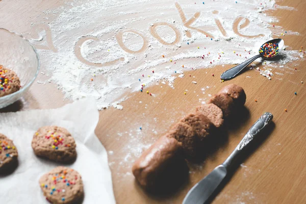 Cookie homemade preparation recipe step ingredients on wooden table flour, cocoa powder, dough pastry and sliced pastry ready to go on baking paper with sweet cookies on the side cookie sign on flour