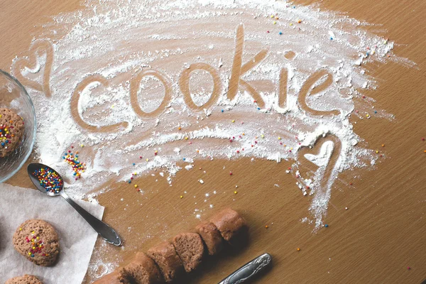 Cookie homemade preparation recipe step ingredients on wooden table flour, cocoa powder, dough pastry and sliced pastry ready to go on baking paper with sweet cookies on the side cookie sign on flour