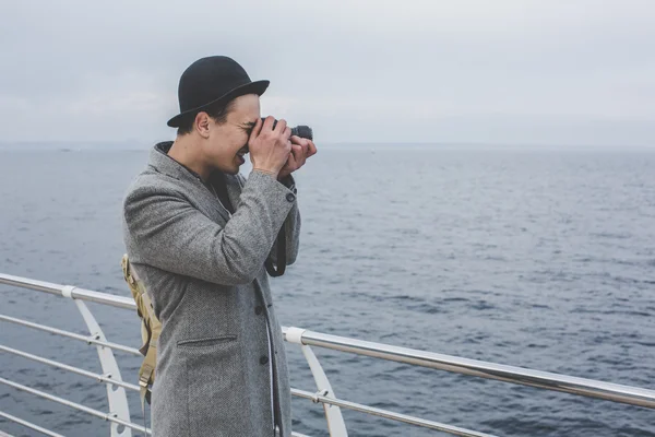 handsome young hipster guy in hat taking picture with film camera of the sea