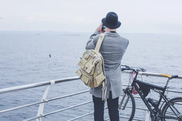 Bonito jovem hipster cara no chapéu tomando foto com filme câmera do mar — Fotografia de Stock