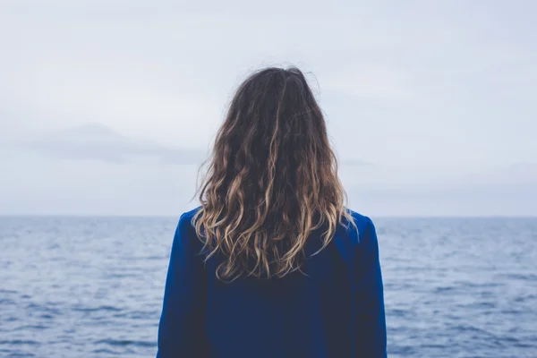 Joven chica rubia rizada mirando el sol brumoso a través de una espesa niebla en un mar tranquilo y cielos azules vista trasera — Foto de Stock