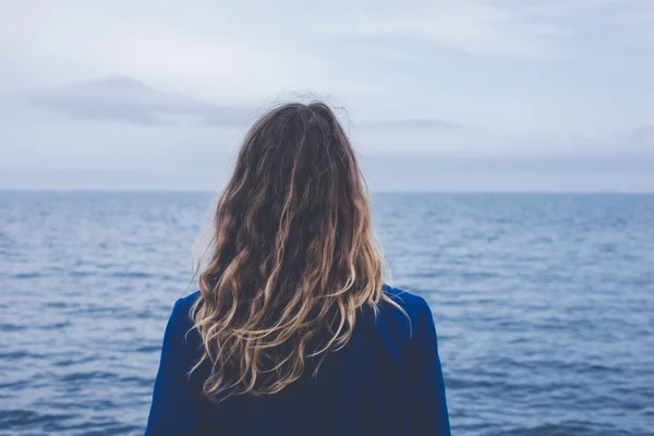 young blonde curly girl looking at hazy sunshine through a thick mist on a calm sea and blue skies back view