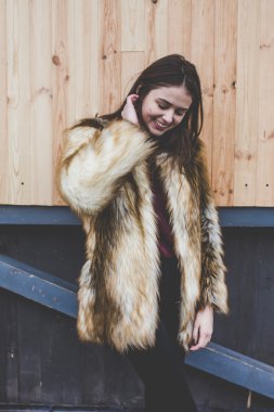 Genç hipster çok güzel beyaz stilysh ve güzel esmer saçlı trendy kız açık havada, cadde ve ahşap serin arka arka plan üzerinde rüzgarlı bahar günü sırasında gülümseyen eğlenceli sahip