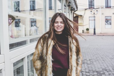 Genç hipster çok güzel beyaz stilysh ve güzel esmer saçlı trendy kız açık havada, cadde ve ahşap serin arka arka plan üzerinde rüzgarlı bahar günü sırasında gülümseyen eğlenceli sahip