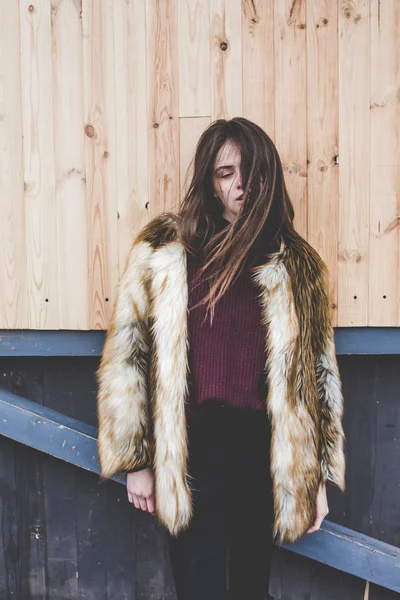 Joven hipster muy hermosa chica caucásica stilysh y de moda con hermoso pelo morena se divierte sonriendo al aire libre en un fondo de las calles y fondos frescos de madera durante el día de primavera ventoso — Foto de Stock