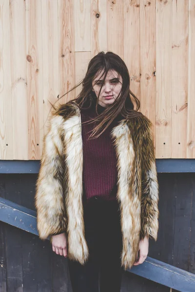 Joven hipster muy hermosa chica caucásica stilysh y de moda con hermoso pelo morena se divierte sonriendo al aire libre en un fondo de las calles y fondos frescos de madera durante el día de primavera ventoso — Foto de Stock