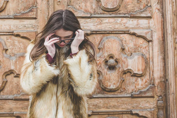 Young hipster very beautiful caucasian stilysh and trendy girl with gorgeous brunette hair is having fun smiling outdoors on a background of the streets and wooden cool backgrounds during windy spring day — Stock Photo, Image