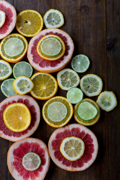 Cutted citrus mix lemon grapefruit lime and orange in geometrical shapes on dark wood rustic background  soft focus overhead-angle shot — Stock Photo, Image