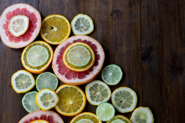 Cutted citrus mix lemon grapefruit lime and orange in geometrical shapes on dark wood rustic background  soft focus overhead-angle shot — Stock Photo, Image