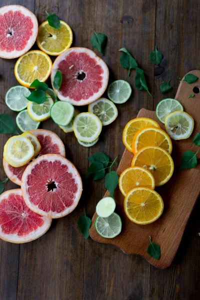 Cutted citrus mix lemon grapefruit lime and orange in geometrical shapes on dark wood rustic background  soft focus overhead-angle shot — Stock Photo, Image