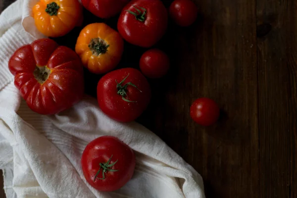 Mix of fresh organic red yellow and cherry tomatoes with water drops from farmers market decorated in rustic style on a dark wood background soft focus overhead-angle shot — Stock Photo, Image