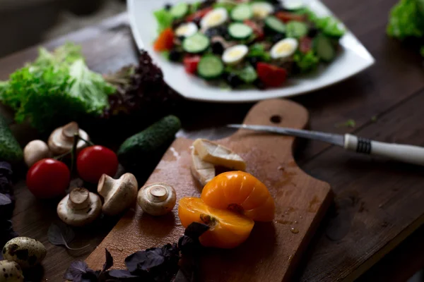 Preparación de ensaladas con huevos de codorniz, champiñones, mezcla de tomates rojos amarillos y cereza, pepino, albahaca, queso brie, lechuga y aceitunas negras, todos orgánicos y frescos del mercado de agricultores en rústico sryle sobre fondo de madera oscura enfoque suave en ángulo superior — Foto de Stock