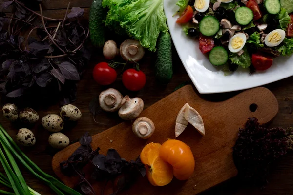 Salad preparation with quail eggs, mushrooms, mix of red yellow and cherry tomatoes, cucumber, basil, brie cheese, lettuce, and black olives all organic and fresh from farmers market in rustic sryle on dark wood backround soft focus overhead-angle — Stock Photo, Image