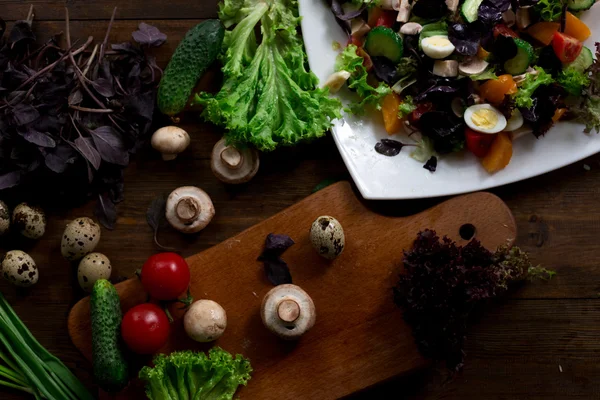 Salad preparation with quail eggs, mushrooms, mix of red yellow and cherry tomatoes, cucumber, basil, brie cheese, lettuce, and black olives all organic and fresh from farmers market in rustic sryle on dark wood backround soft focus overhead-angle — Stock Photo, Image