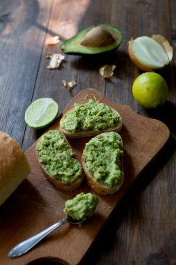 hazırlanması sürecinde avokado guacamole tablo kireç, soğan, avokado tüm organik ve taze koyu ahşap rustik tarzı arka plan üzerinde bir taze pişmiş ciabatta üzerinde hazır guacamole ile tüm ingridients yumuşak odak ek yük-açısı shot ekmek.