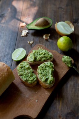 hazırlanması sürecinde avokado guacamole tablo kireç, soğan, avokado tüm organik ve taze koyu ahşap rustik tarzı arka plan üzerinde bir taze pişmiş ciabatta üzerinde hazır guacamole ile tüm ingridients yumuşak odak ek yük-açısı shot ekmek.