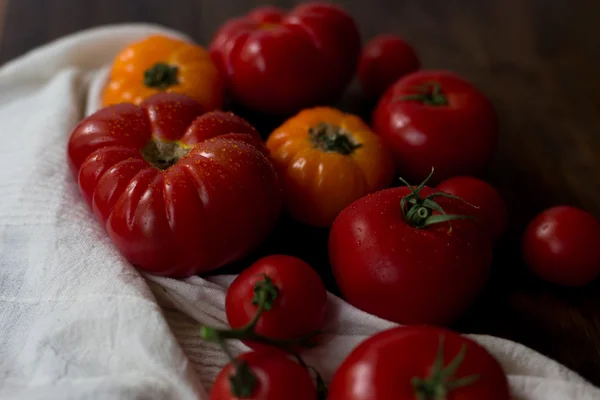 Mezcla de tomates rojos y cereza orgánicos frescos con gotas de agua del mercado de agricultores decorados en estilo rústico sobre un fondo de madera oscura enfoque suave tiro de ángulo superior — Foto de Stock