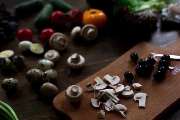 Préparation de salade avec des œufs de caille, champignons, mélange de tomates rouges jaunes et cerises, concombre, basilic, fromage de brie, laitue et olives noires tous biologiques et frais du marché fermier en sryle rustique sur fond de bois foncé focus doux angle supérieur — Photo