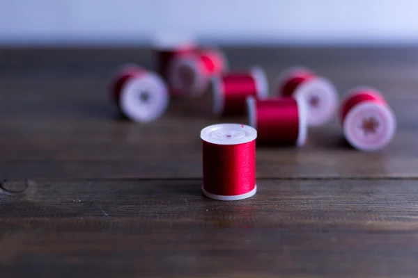 Červené nitě pro vyšívání a šití složení na tmavé dřevo stůl rustikální — Stock fotografie