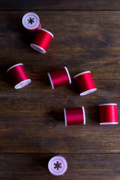 Red threads for embroidery and sewing composition on dark wood table rustic — Stock Photo, Image