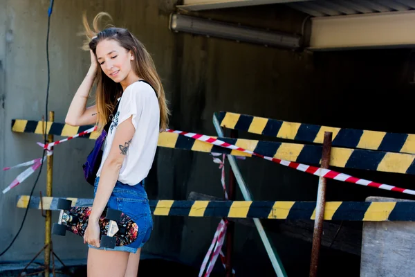 Cool young and beautiful caucasian blonde hipster skater girl wearing denim shorts posing smiling and having fun outside while skating with her cute little skateboard during amazing summer day — Stock Photo, Image