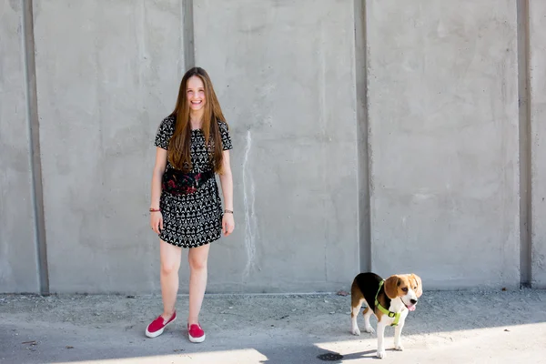 Retrato de fresco joven y hermosa rubia caucásica adolescente hipster chica con el pelo largo y hermoso está posando sonriente y divertirse con su perro perrito beagle — Foto de Stock