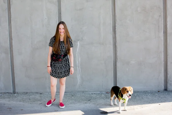 Portrait of cool young and beautiful caucasian blonde teenager hipster girl with long gorgeous hair is posing smiling and having fun with her beagle puppy dog — Stock Photo, Image