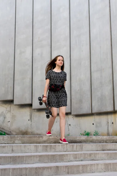 Cool young and beautiful caucasian blonde teenager hipster skater girl with long gorgeous hair is posing smiling and having fun outside while skating with her cute little skate during amazing summer day — Stock Photo, Image