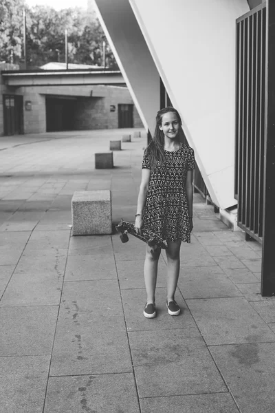 Fresco joven y hermosa caucásica rubia adolescente hipster skater chica con el pelo largo y hermoso está posando sonriente y divertirse al aire libre mientras patina con su pequeño patín lindo durante el increíble día de verano — Foto de Stock