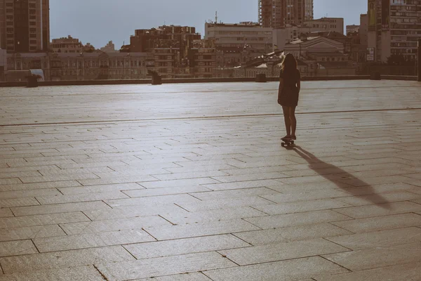 Fresco joven y hermosa caucásica rubia adolescente hipster skater chica con el pelo largo y hermoso es patinar durante la puesta del sol en un fondo de paisaje urbano — Foto de Stock