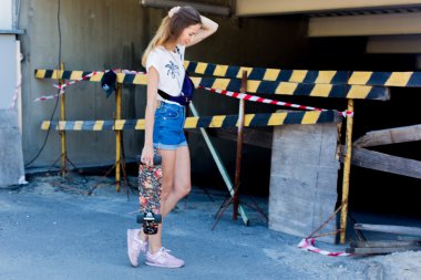 gülümseyen ve onun sevimli küçük kaykay ile şaşırtıcı yaz gün boyunca paten yaparken eğlenmek dışında poz kot şort giyen havalı genç ve güzel beyaz sarışın hipster patenci kız