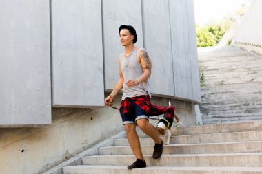 gülümseyen ve having fun dışında inanılmaz yaz gün boyunca şehrin onun beagle yavru köpek ile poz bir şapka giyen havalı genç ve yakışıklı beyaz esmer hipster adam