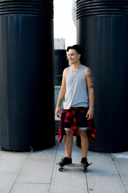 gülen ve having fun dışında kaykayıyla şaşırtıcı yaz gün boyunca şehirde buz pateni yaparken poz bir şapka giyen havalı genç ve yakışıklı beyaz esmer hipster patenci adam