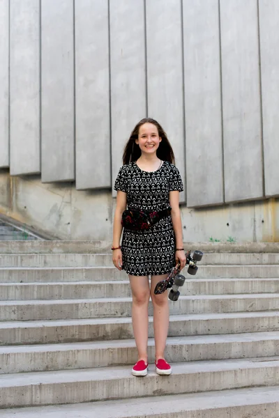 Fresco joven y hermosa caucásica rubia adolescente hipster skater chica con el pelo largo y hermoso está posando sonriente y divertirse al aire libre mientras patina con su pequeño patín lindo durante el increíble día de verano — Foto de Stock