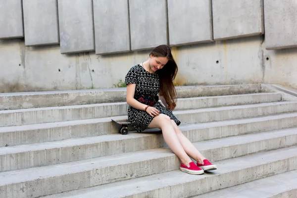 Fresco joven y hermosa caucásica rubia adolescente hipster skater chica con el pelo largo y hermoso está posando sonriente y divertirse al aire libre mientras patina con su pequeño patín lindo durante el increíble día de verano — Foto de Stock