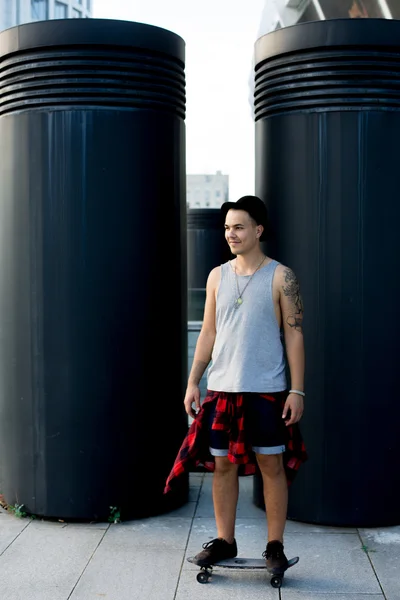 Legal jovem e bonito caucasiano morena hipster skater cara vestindo um chapéu posando sorrindo e se divertindo fora enquanto patina com seu skate durante incrível dia de verão na cidade — Fotografia de Stock