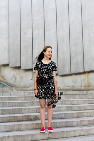 Cool young and beautiful caucasian blonde teenager hipster skater girl with long gorgeous hair is posing smiling and having fun outside while skating with her cute little skate during amazing summer day — Stock Photo, Image