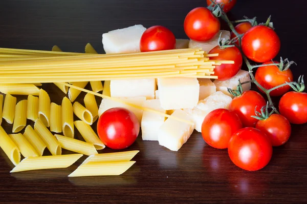 Italian grana padano, pasta and tomatoes on dark wood background — Stock Photo, Image