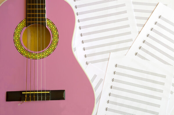 Фиолетовая гитара для детей с скрипичным ключом на фоне нот
