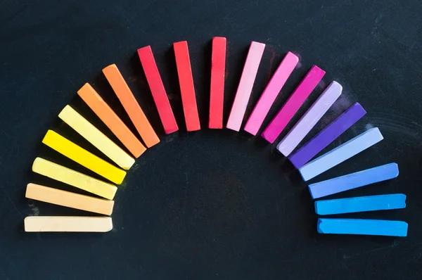 Rainbow of colorful chalks lined up rounded on circle on blackboard — Stock Photo, Image