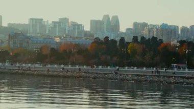 İnsanlar ve gezginler Bakü Bulvarı 'nda yürüyor, konuşuyor ya da eğleniyorlar. Soğuk ruh hali, martılar ve görkemli günbatımı anı. Bakü, Azerbaycan. 13.12.2025.