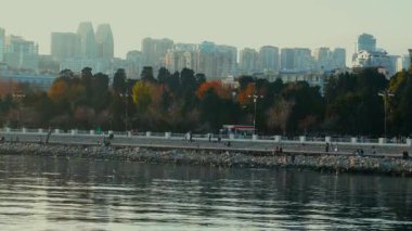 İnsanlar ve gezginler Bakü Bulvarı 'nda yürüyor, konuşuyor ya da eğleniyorlar. Soğuk ruh hali, martılar ve görkemli günbatımı anı. Bakü, Azerbaycan. 13.12.2025.