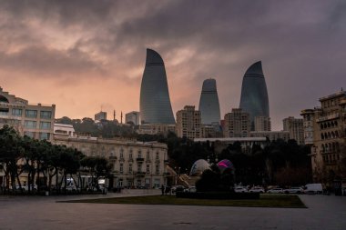 Kasvetli bir gökyüzü altında Bakü 'nün dramatik şehir manzarası cesur mimari, canlı şehir enerjisi ve Azerbaycan başkentinin dinamik ruhunu sergiliyor..
