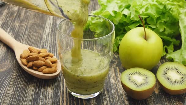 Donna che versa un succo verde di disintossicazione dal frullatore al barattolo, a casa indossando abiti sportivi . — Video Stock